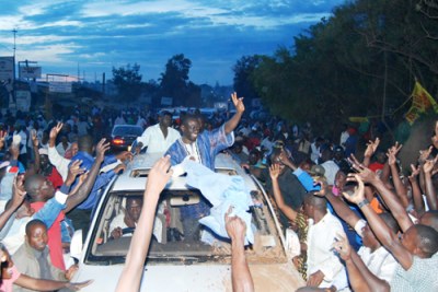Kizza Besigye, atop a car, waves to supporters after he was granted bail during an earlier hearing.