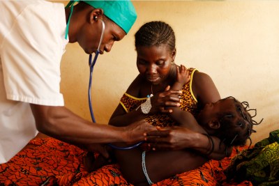 Health care worker examines a child in l'Auberge de l'Amour Rédempteur clinic, Benin.