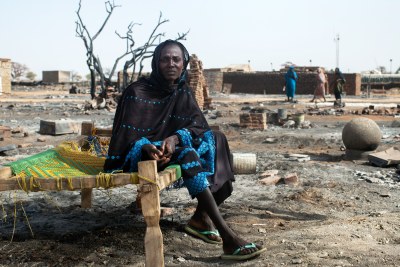 A displaced woman sits on a bed next to the remnants of her burnt house in Khor Abeche, South Darfur.