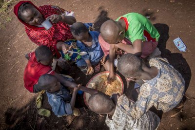 Six boys tuck into a bowl of food as Ramatou sips water from a cup in Mbile Refugee Camp, CAR.