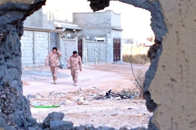 Two soldiers from forces operating under Libya's Tripoli-based government walking through the deserted streets of Bin Jawad, seen through a hole blown in the outside wall of a family home (file photo).