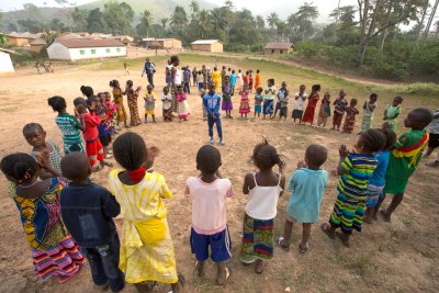 Des enfants, encadrés par un adulte, jouent dans le village de Meliandou